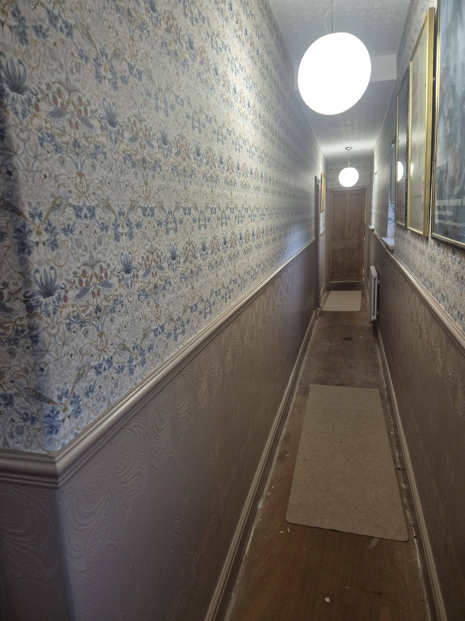 Long hallway finished with patterned wallpaper above a painted dado rail